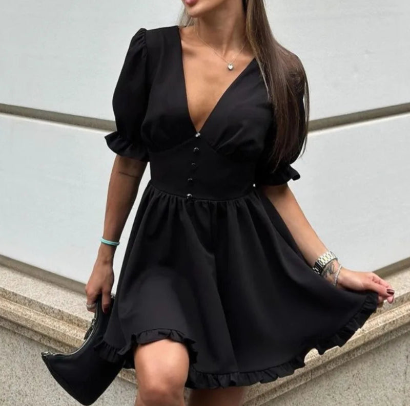 Woman wearing a black dress standing against a light-colored wall.