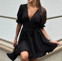 Woman wearing a black dress standing against a light-colored wall.