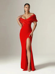 Woman wearing a red off-shoulder gown with a high slit on a plain background
