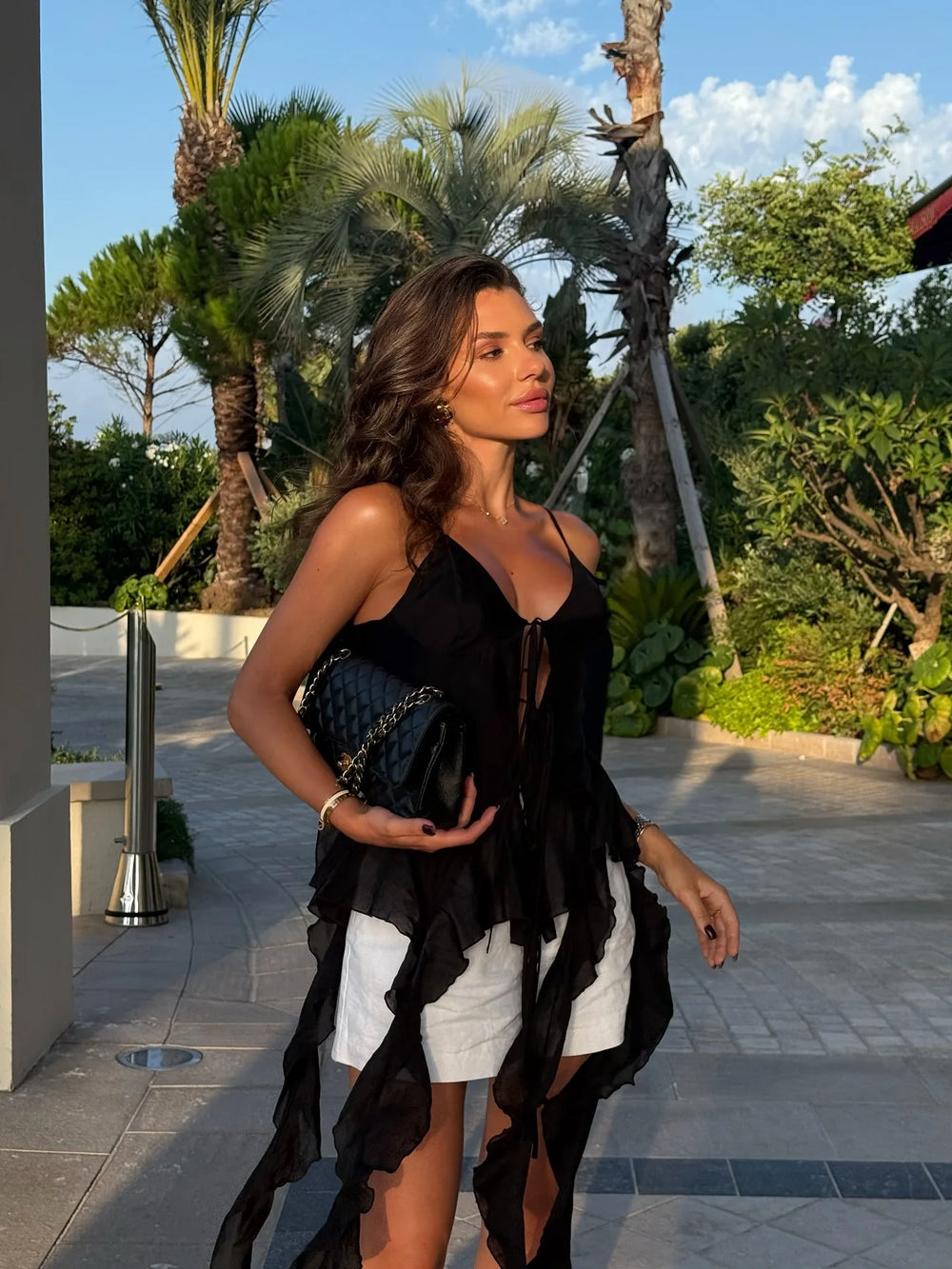 Woman in black top and white shorts walking outdoors with palm trees in the background