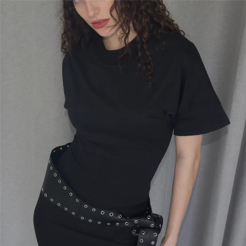 Person wearing a black t-shirt and black pants with silver studs against a gray background