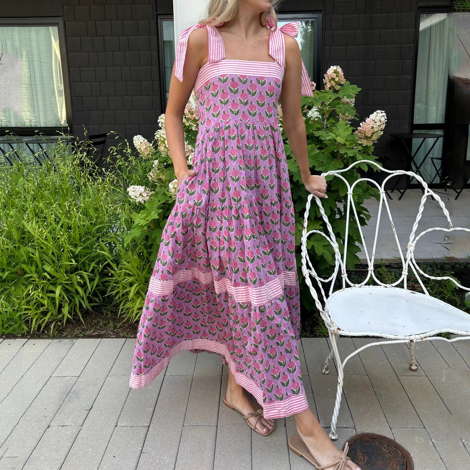 Woman in a pink dress with floral pattern standing on a wooden deck.