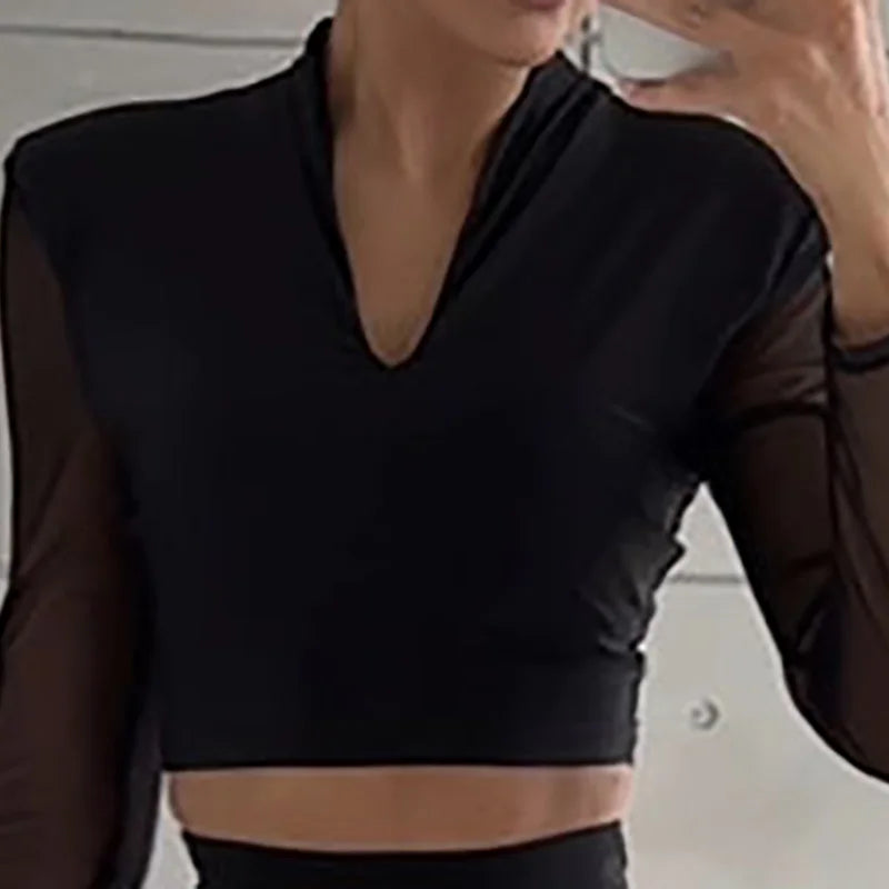 Person wearing a black long-sleeve top with sheer sleeves against a neutral background