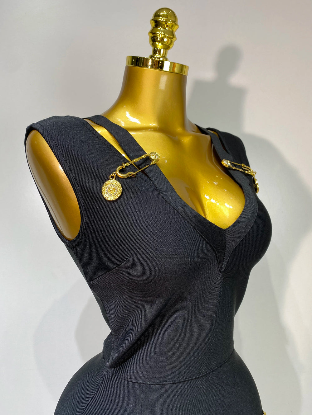 Black dress on a mannequin with gold accents against a white background