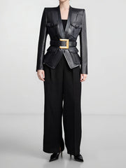 Person wearing a black leather jacket with gold buckle and black pants on a light gray background