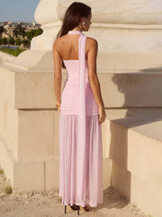 Woman in a pink dress standing against a stone wall with a scenic background