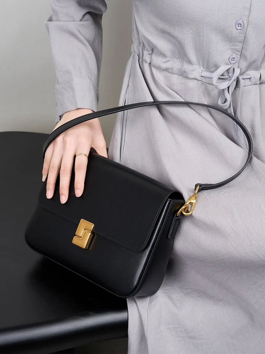 Person holding a black handbag with a gold clasp against a neutral background