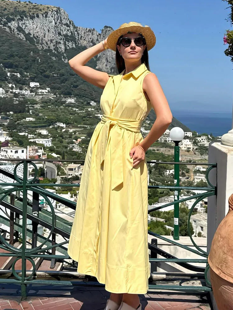 Woman in a yellow dress and hat standing on a scenic balcony with ocean view