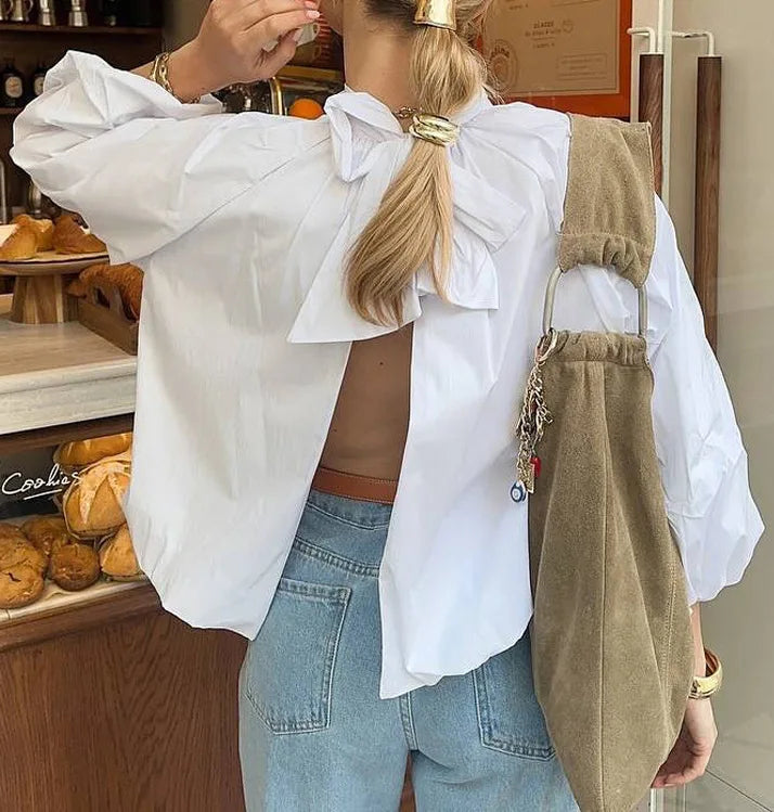Person wearing a white shirt and blue jeans with a beige bag, standing in a bakery.
