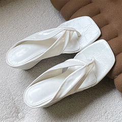 Pair of white square toe wedge flip flops on a textured surface