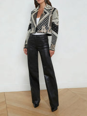 Person wearing a patterned jacket and black leather pants against a white wall.