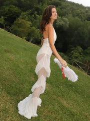 Woman in a white dress standing on a grassy hill with trees in the background