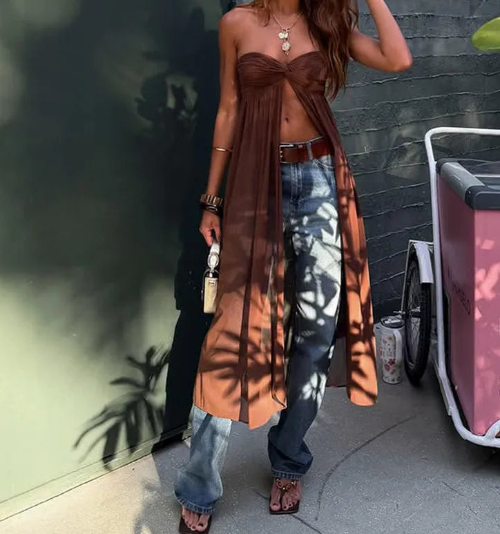 Woman in a strapless brown top and jeans standing against a wall with a pink cart in the background.