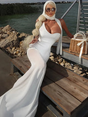 Woman in a white dress sitting on a boat with water and rocks in the background