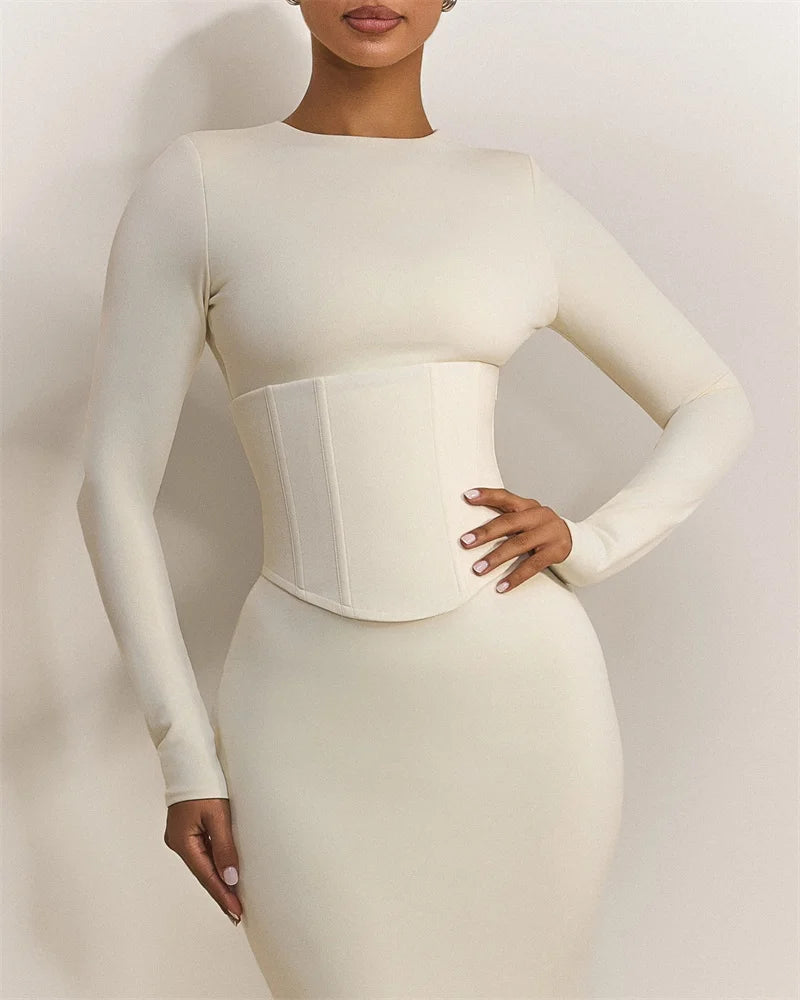 Woman wearing a fitted white dress with a waistband against a plain background