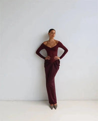A person posing in an off shoulder long sleeve maxi dress with ruched waist detail against a white wall.