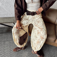 Person wearing white lace pants and a brown jacket, holding a brown handbag.