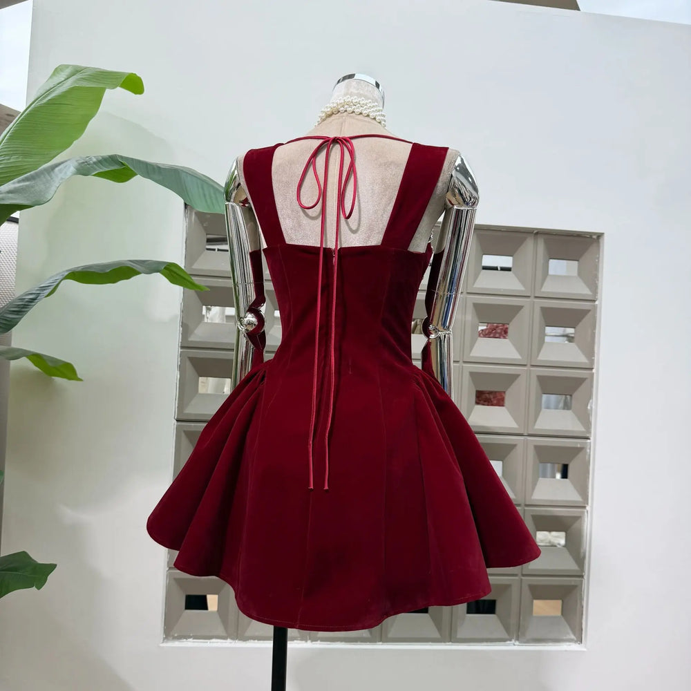 Red dress on a mannequin against a white wall with a plant to the left.