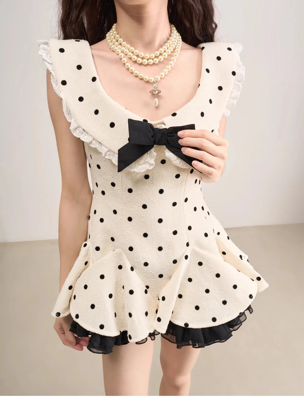 Woman wearing a polka dot dress with a black bow and pearl necklace on a plain background
