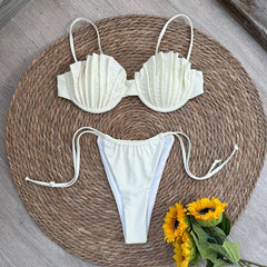 Person wearing a white bikini with shell-shaped cups and tie-side bottoms on a sandy beach.