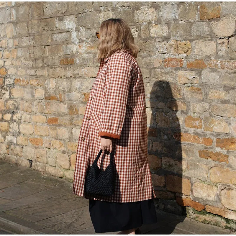Person wearing a checkered coat standing against a stone wall