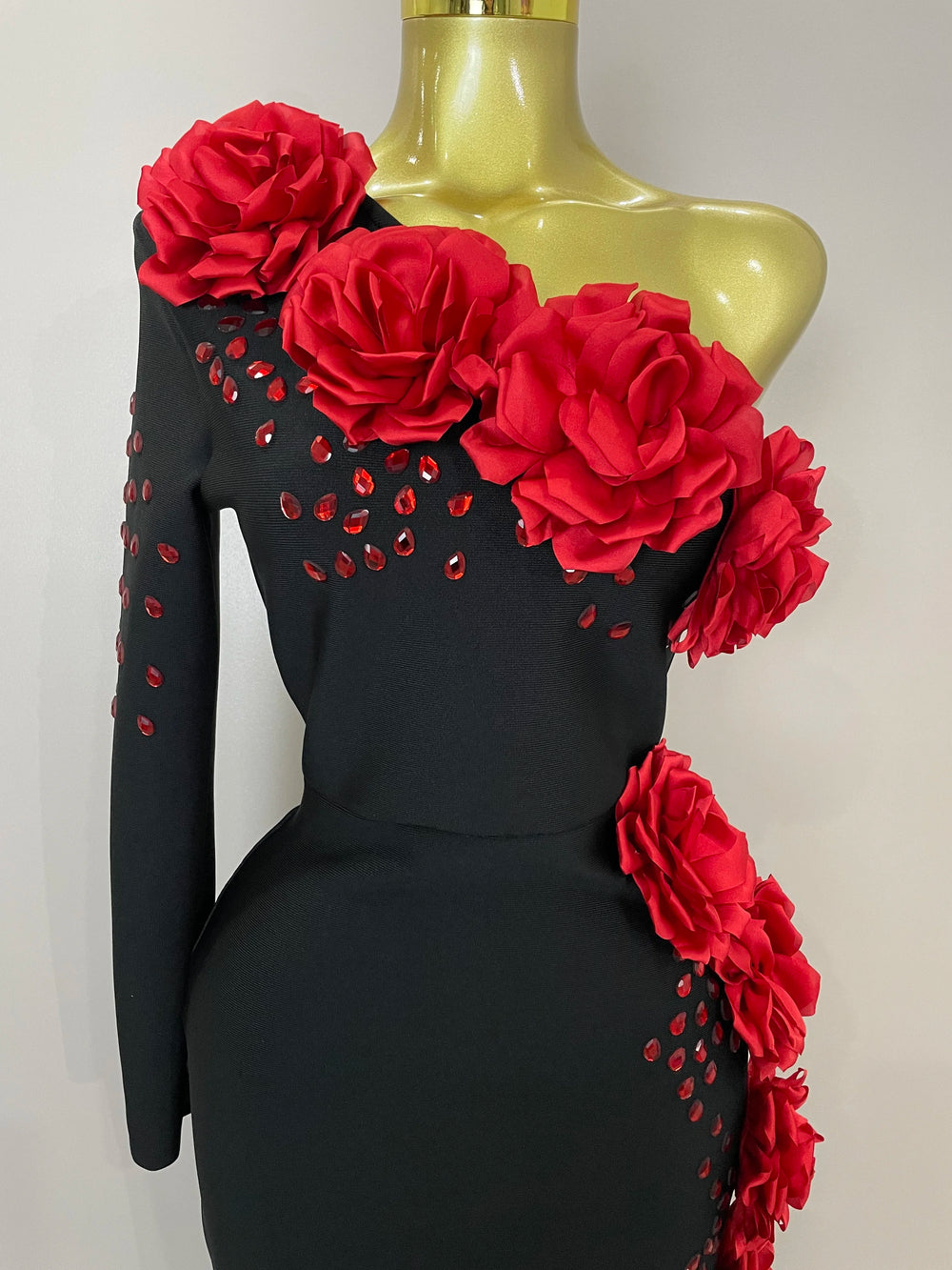 Black dress with red floral embellishments on a mannequin against a white background