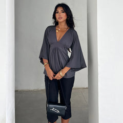 Woman wearing a gray top and black pants, holding a black handbag with a white logo.