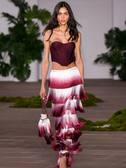 Model wearing a burgundy top and ruffled skirt with a gradient design on a runway.