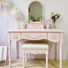 Pink vanity table with mirror, lamp, and decorative items in a room.