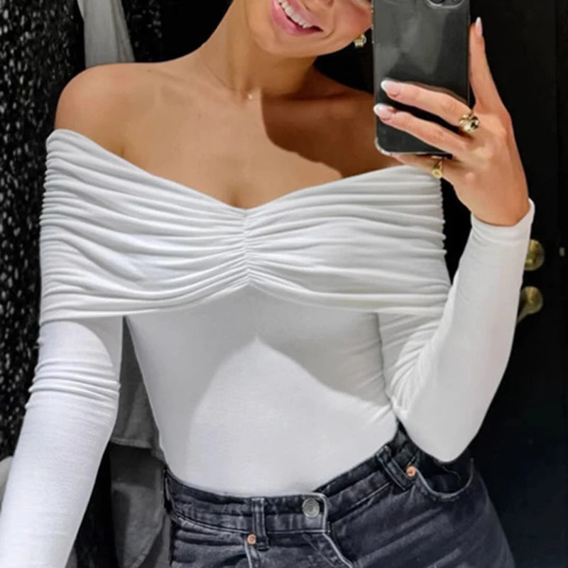 Woman wearing a white off-shoulder top and dark jeans, taking a selfie.