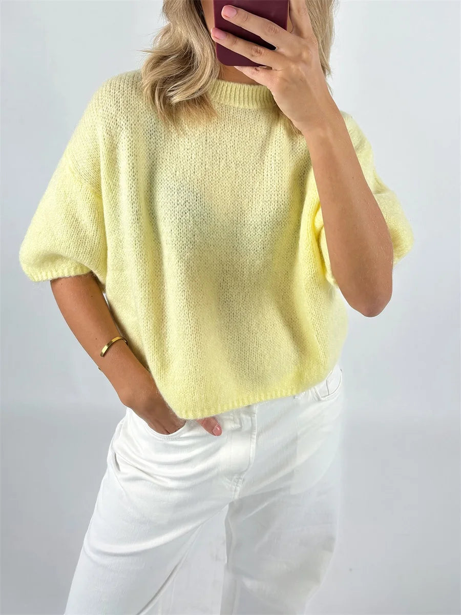 Person wearing a yellow knit sweater and white pants against a plain background