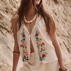 Woman wearing a white embroidered top with floral designs against a rocky background