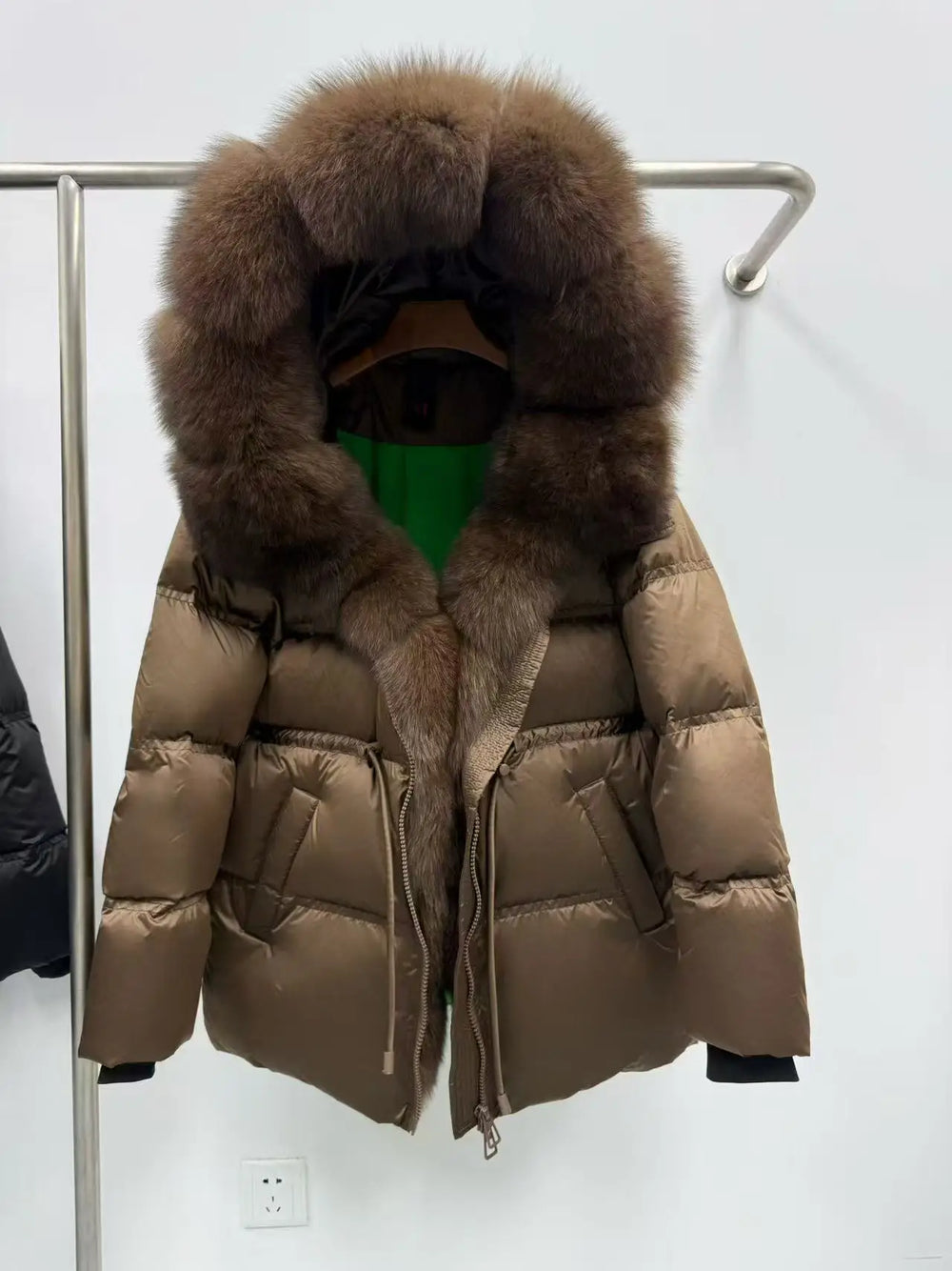 Brown puffer jacket with fur hood on a rack against a white background