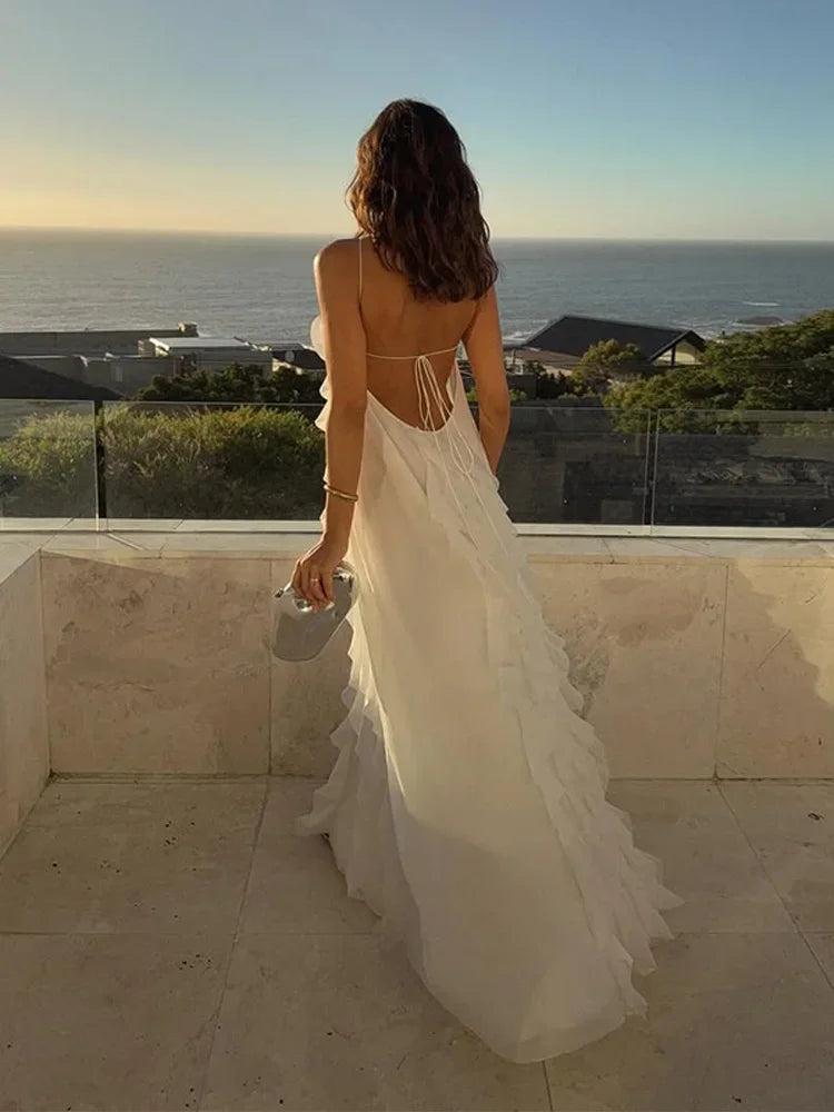Woman in a white dress standing on a balcony overlooking the ocean.