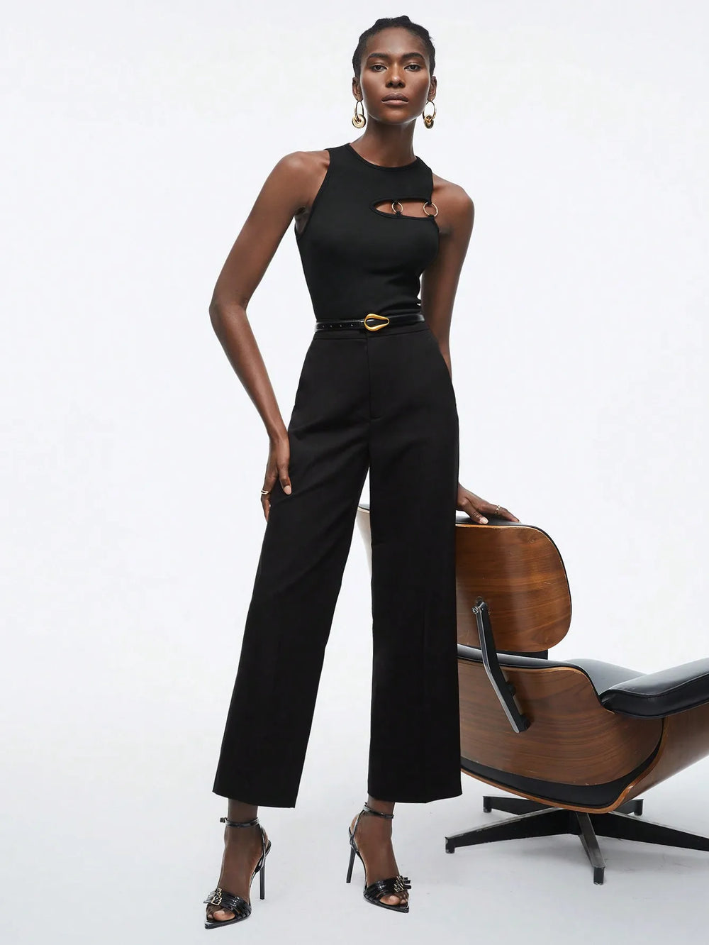 Woman in a black jumpsuit standing next to a wooden chair 