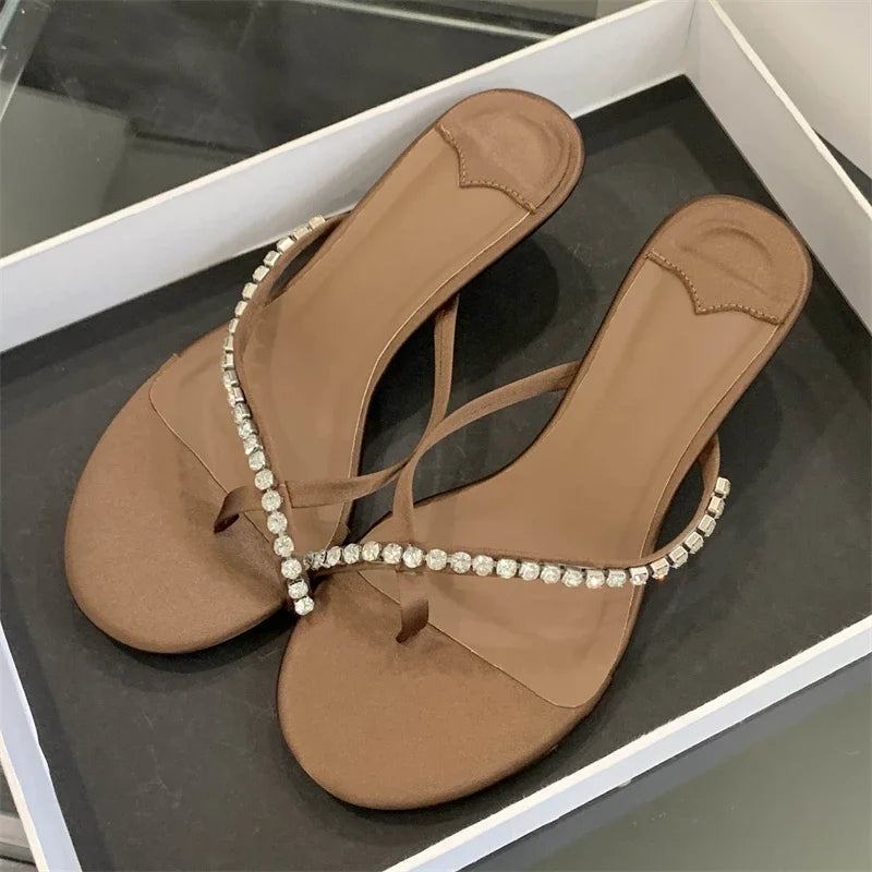 Pair of brown sandals with decorative straps on a reflective surface