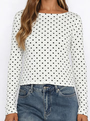 White long-sleeve top with black polka dots worn by a person, paired with blue jeans.