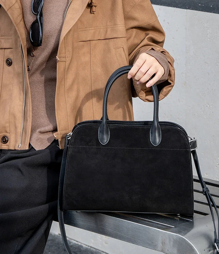Person holding a black handbag with a neutral background
