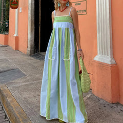 Woman wearing a long, colorful dress with a striped pattern in front of an orange building.