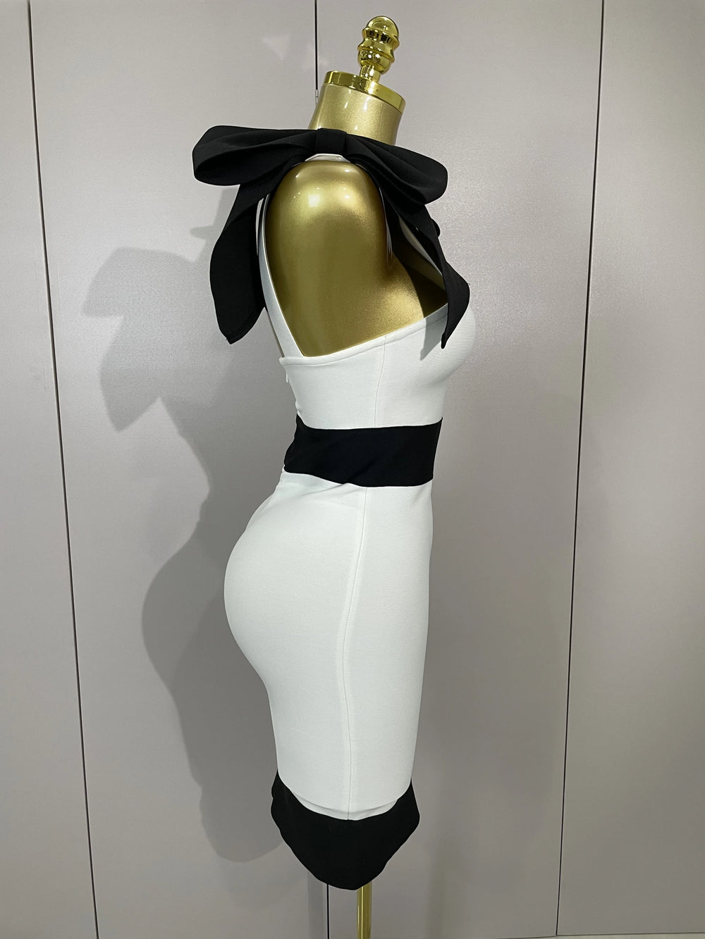 Mannequin with gold head and white body wearing a black bow tie against a plain background
