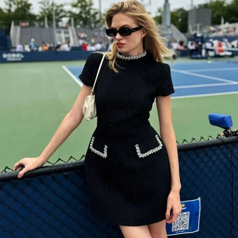 Woman in a black dress with decorative elements standing on a tennis court.