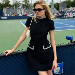Woman in a black dress with decorative elements standing on a tennis court.