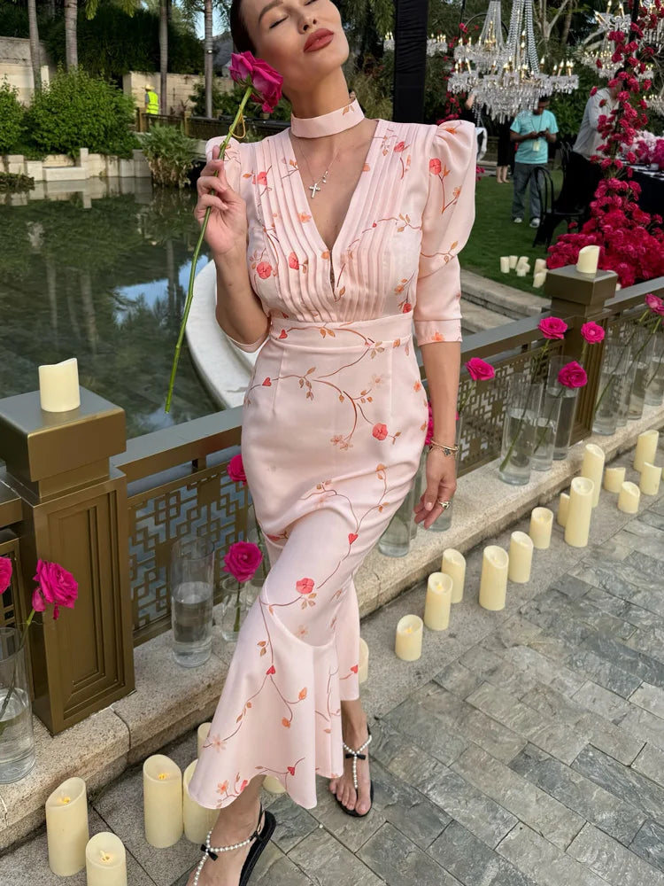 Woman in a pink floral dress standing outdoors with candles and flowers around.