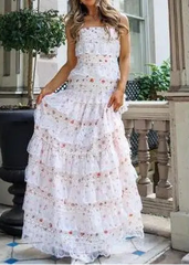 Woman wearing a white floral dress standing in an outdoor setting with plants and furniture.