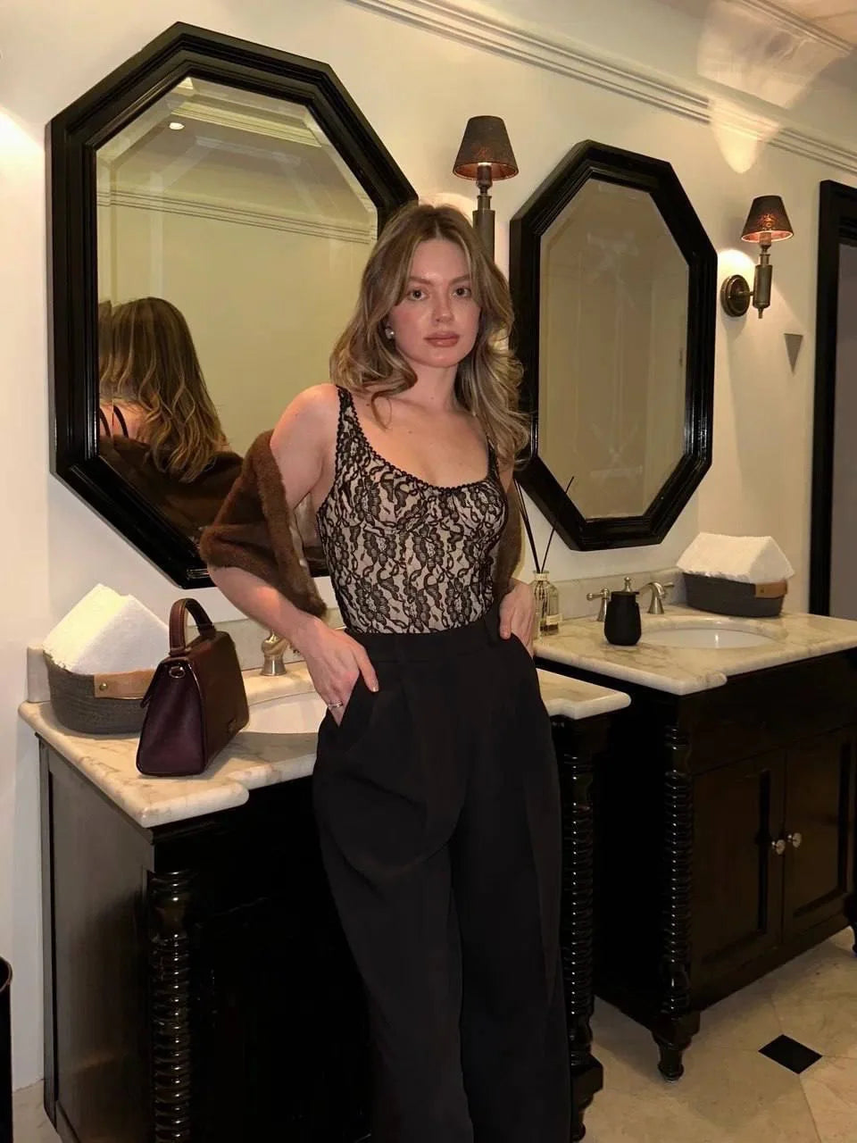 Woman standing in a bathroom with large mirrors and a sink.