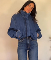 Person wearing a blue denim jacket and jeans against a plain background