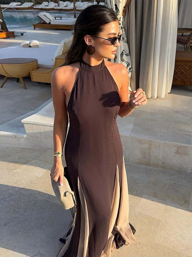 Woman in a brown halter neck dress standing by a poolside.