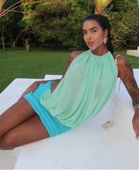 Woman lounging in a halter ruched mesh mini dress.