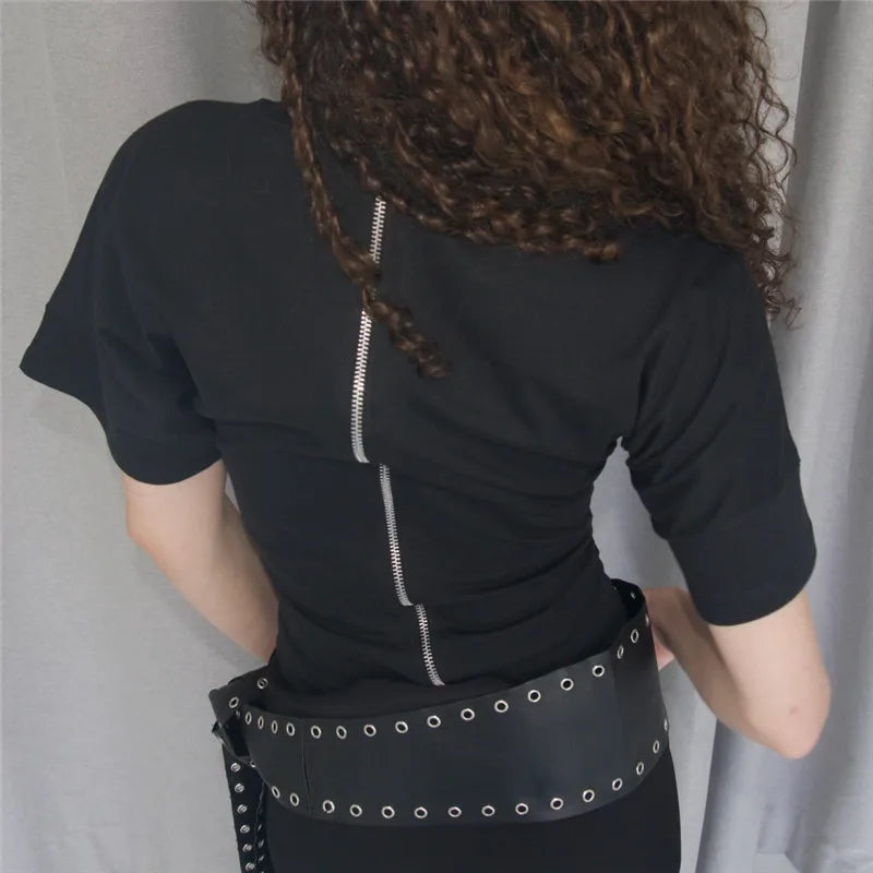 Person wearing a black outfit with a belt featuring eyelets against a neutral background