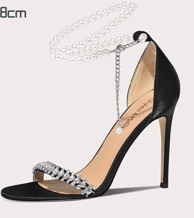 Black high-heeled shoe with crystal embellishments on a light gray background